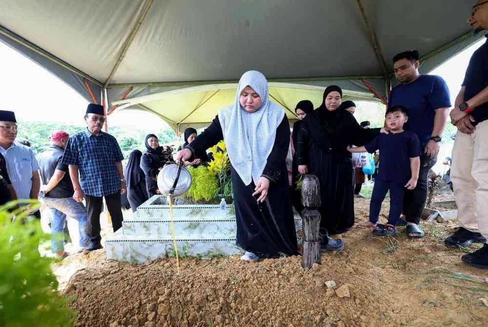 Nurhafizah Fatin menyiram air ke atas pusara bapanya di Tanah Perkuburan Islam Taman Bintang Baru Rancangan Sungai Manila pada Isnin. Foto Bernama