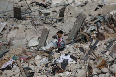 Seorang kanak-kanak lelaki Palestin berdiri di atas runtuhan bangunan di kawasan kejiranan yang musnah di bandar selatan Gaza, Rafah pada Isnin, ketika penduduk kembali selepas perjanjian gencatan senjata bermula pada Ahad. (Foto oleh Eyad BABA / AFP)
