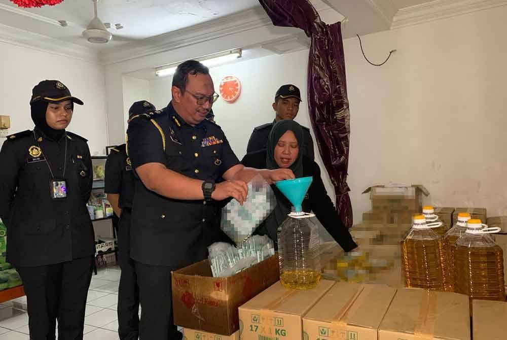 Lilis Saslinda (kanan) menunjukkan minyak masak yang diseleweng hasil serbuan di Taman Mewah Johor Bahru pada Rabu.