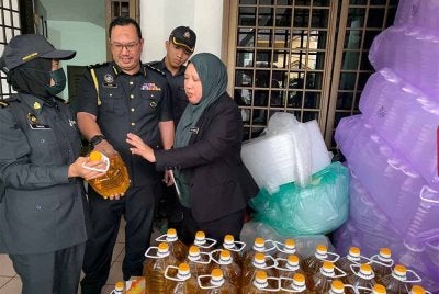 Lilis Saslinda (kanan) menunjukkan minyak masak yang diseleweng hasil serbuan di Taman Mewah Johor Bahru pada Rabu.