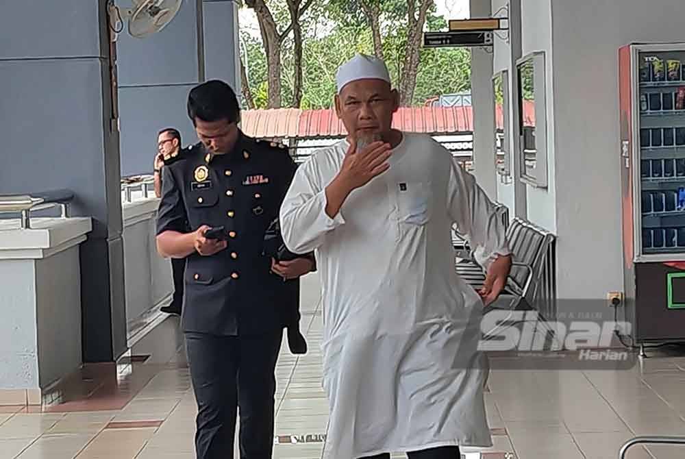 Azizul diiring pegawai KPDN ketika hadir ke mahkamah.