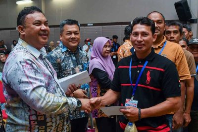 Azman (kiri) menyampaikan sumbangan kepada penerima pada Program Bantuan One-Off Perdana Menteri di Dewan Kelab Suara Muda pada Khamis. Foto Bernama