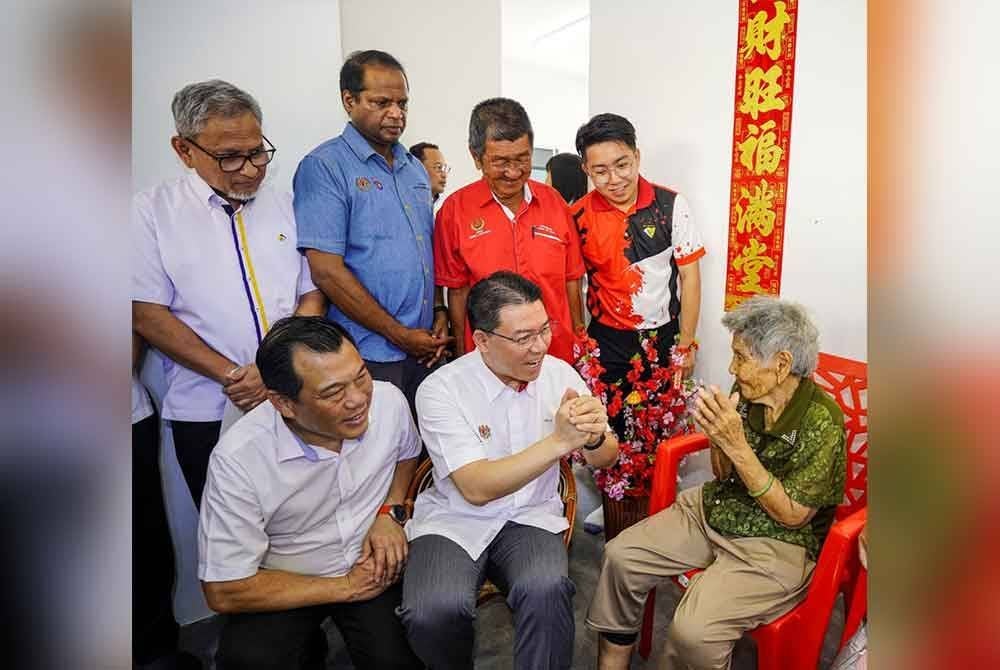 Kor Ming (duduk, tengah) menyantuni warga emas, Liew Keow, 92, dari Kampung Baru Rimba Panjang, Sungai Siput yang menerima bantuan bina rumah baharu di bawah Program Rumah Madani Rakyat Kampung Baru.