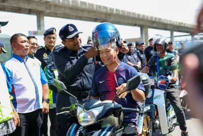 Hussein (tengah) memakaikan topi keledar baharu kepada penunggang motosikal semasa majlis pelancaran kempen keselamatan jalan raya dan advokasi sempena perayaan Tahun Baharu Cina di Plaza Tol PJS 2, Lebuhraya New Pantai Expressway (NPE), Petaling Jaya pada Sabtu. FOTO: BERNAMA