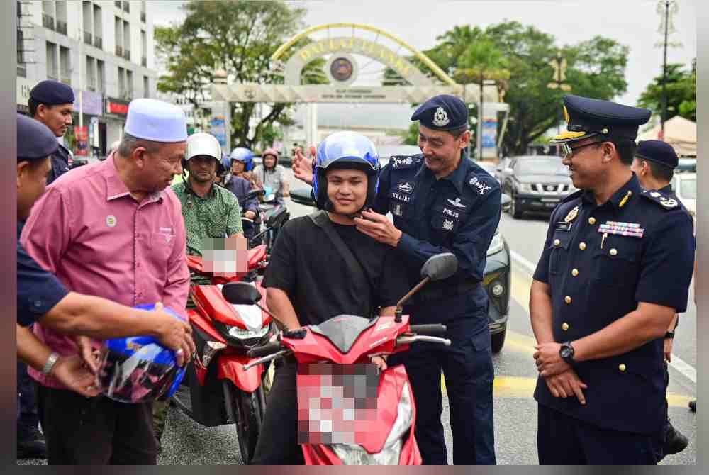 Mohd Khairi (dua dari kanan) memperkemaskan pemakaian topi keledar seorang penunggang motosikal ketika Kempen Keselamatan Jalan Raya Tahun Baru Cina 2025 Peringkat Negeri Terengganu di Dataran Shah Bandar