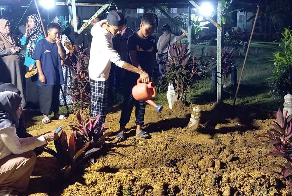 Anak mangsa, Mohd Danial Ikmal (kiri) dan Mohd Danial Irfan (kanan) menyiram air di pusara ibu bapa mereka di Tanah Perkuburan Islam Masjid Darul 'Ulum Merbau Pulas, di sini.