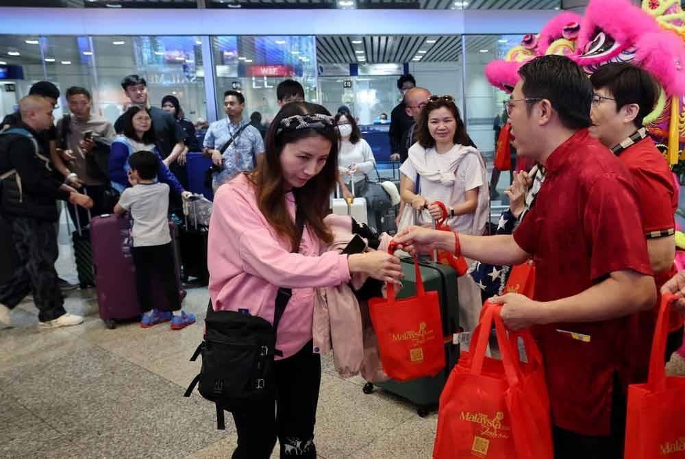 Thai Hung menyerahkan cenderahati kepada pelancong luar dan tempatan yang baru tiba pada Majlis Keraian Sambutan Tahun Baharu Cina 2025 di Lapangan Terbang Antarabangsa Kulala Lumpur (KLIA) Terminal 1 hari ini. - Foto: Bernama