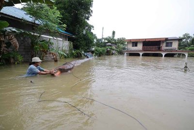 Penduduk mengalihkan batang kayu di hadapan rumahnya di Kampung Hulu Serian yang dilanda banjir pada Khamis. Foto Bernama