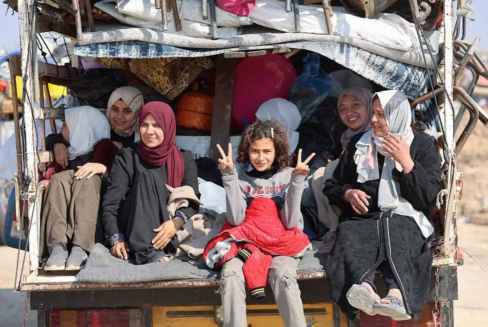 Sekumpulan kanak-kanak dan wanita Palestin duduk di belakang trak ketika mereka melakukan perjalanan pulang menuju ke utara Genting Gaza. - AFP