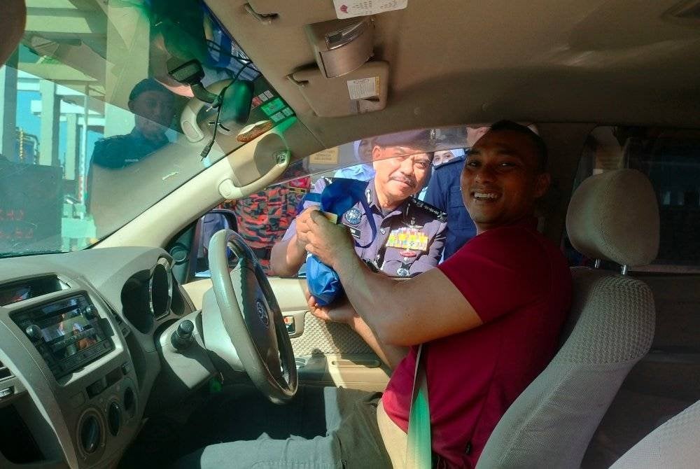 Hamzah (kiri) menyampaikan cenderahati kepada pengguna jalan raya sempena Program Advokasi sempena Op Selamat 23/2025 Tahun Baharu Cina Peringkat PDRM Kontinjen Pulau Pinang di Plaza Tol Sungai Dua arah Selatan di Sungai Dua pada Jumaat.