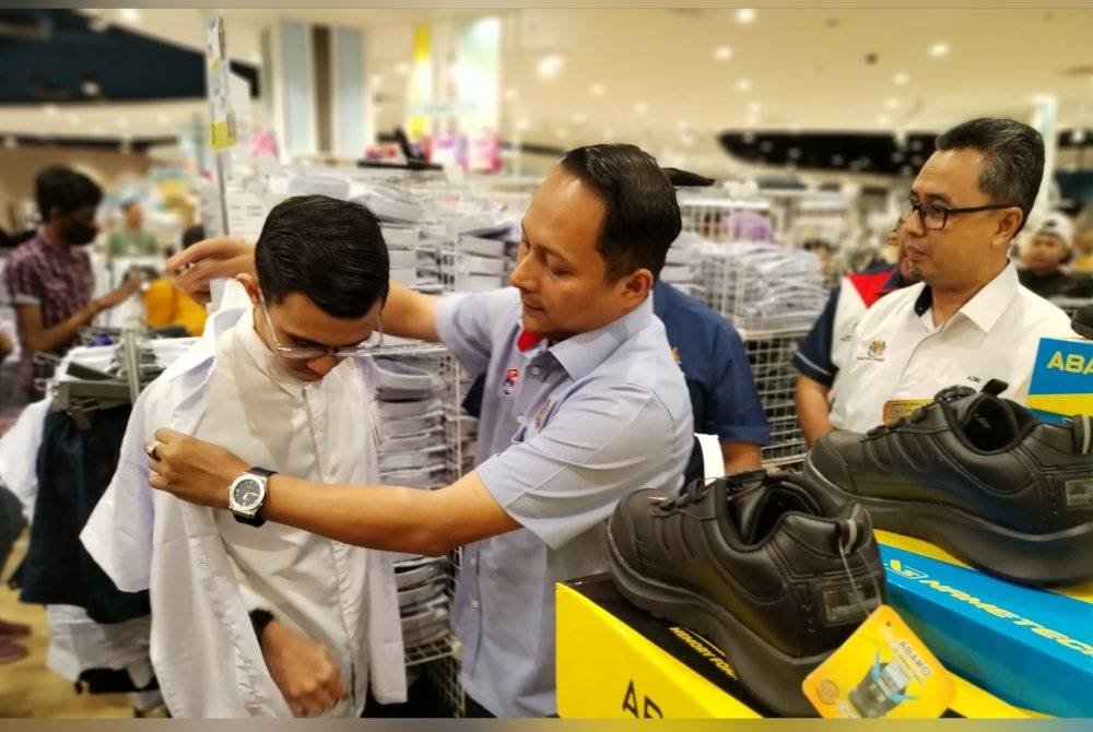 Aznan mengenakan pakaian seragam sekolah kepada salah seorang pelajar sempena Program Bantuan Kasih Murid Johor di AEON Mall Tebrau hari ini.