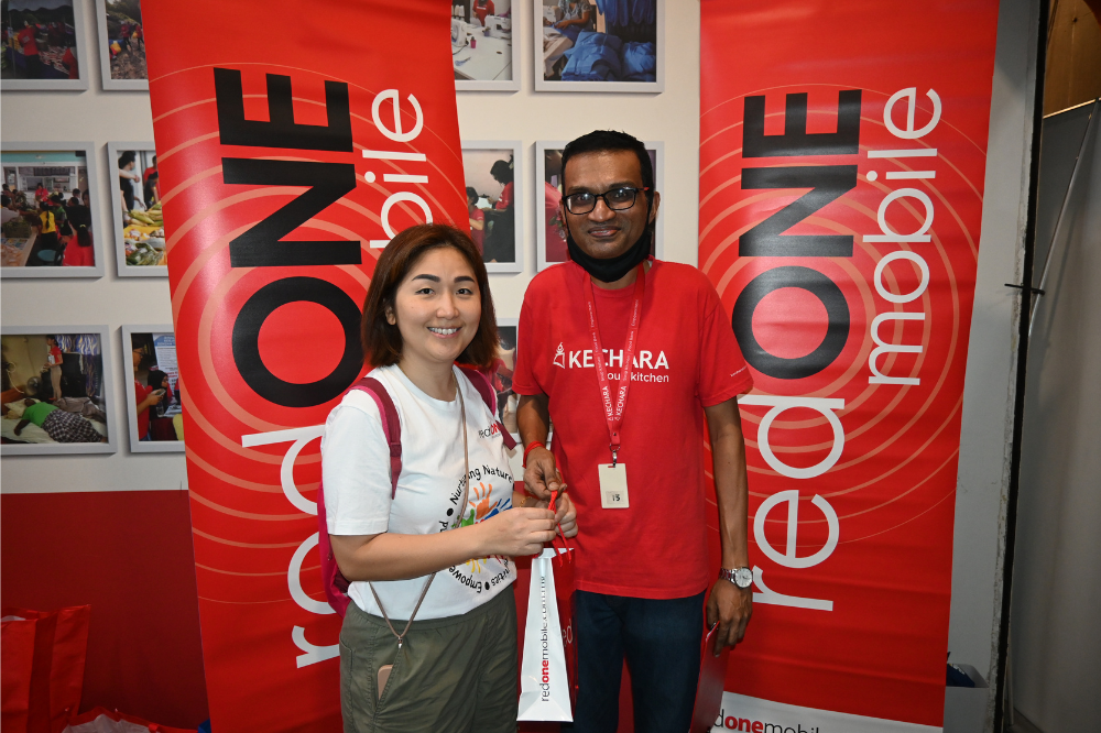 Ketua Tadbir Urus Korporat redONE Mobile, Caren Lwee (kiri) menyampaikan cenderahati kepada wakil Kechara Soup Kitchen, Eswaran Kandasamy sebagai menghargai usaha mereka menyediakan makanan untuk golongan gelandangan di Kuala Lumpur.