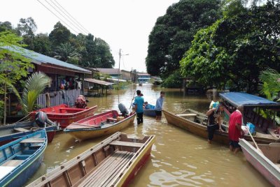 Penduduk kampung menggunakan bot untuk keluar dari rumah mereka selepas kawasan rumah mereka dinaiki air banjir di Pangkalan Buit Garam, Kinabatangan hari ini. Foto Bernama