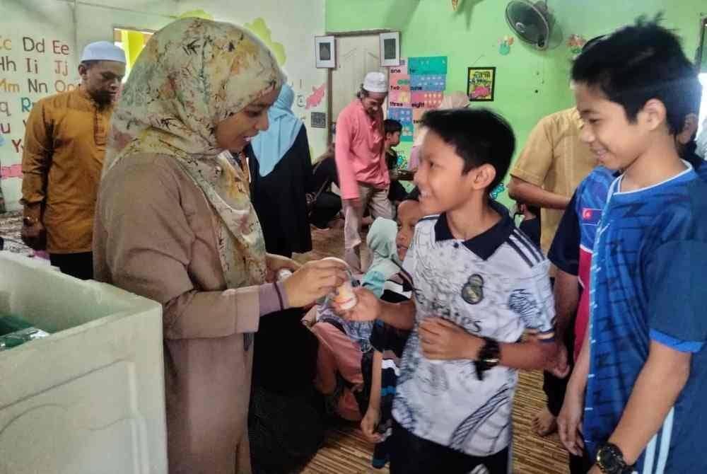 Nik Rozianee (kiri) menyampaikan minuman probiotik kepada kanak-kanak pada Program Sumbangan Beg Sekolah Percuma Oleh Persatuan Kampung Bandar Tercinta pada Rabu.