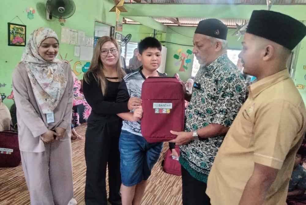 Ahmad Amry Mukhsynin (kanan) mengiringi Azhar menyampaikan beg sekolah kepada penerima bantuan pada Rabu.