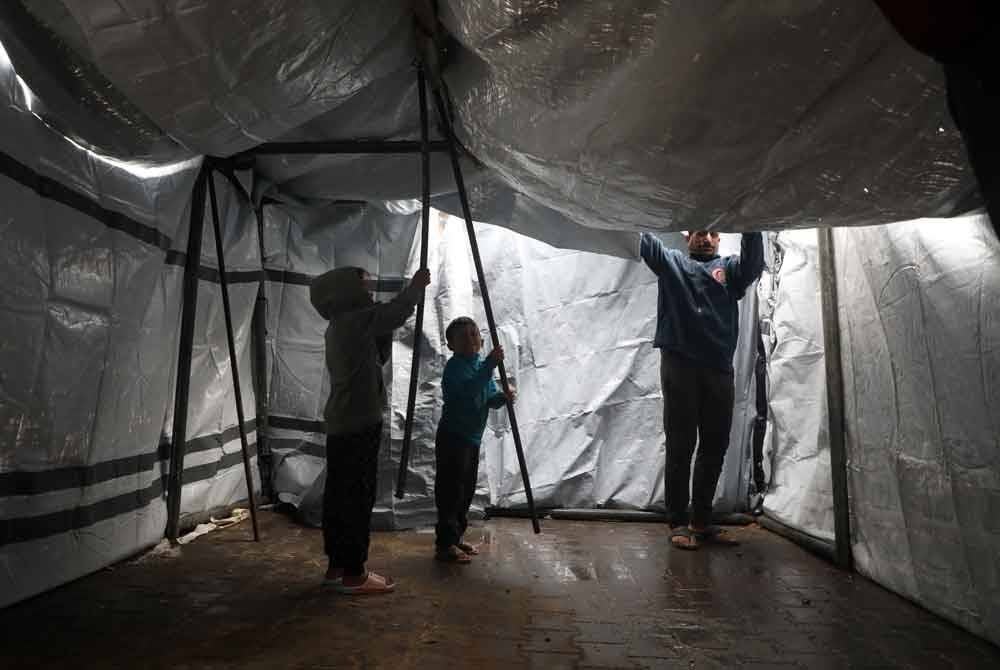 Penduduk cuba membaiki khemah yang rosak akibat hujan lebat di Bandar Gaza. Foto Xinhua