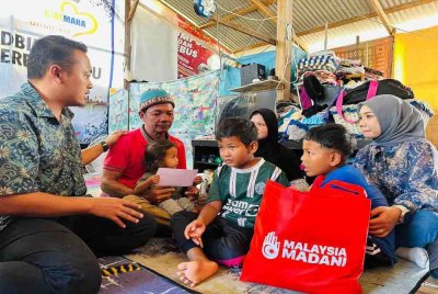 Md Asyraf (kiri) menghulurkan bantuan tunai dan barangan dapur kepada keluarga berkenaan di Kampung Darat Batu Rakit, Kuala Nerus.