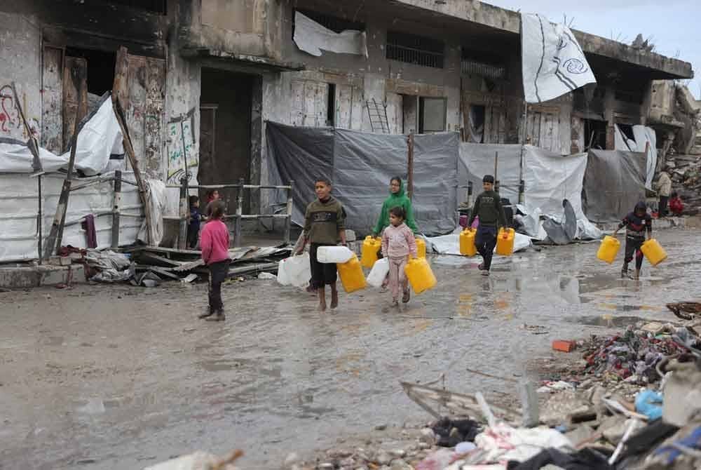 Kanak-kanak Palestin yang kehilangan tempat tinggal membawa botol plastik melintasi jalan berlumpur untuk mengisi air untuk kegunaan harian di khemah mereka.