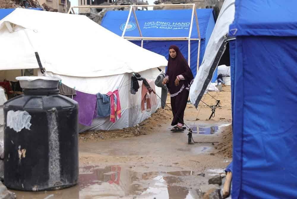 Seorang wanita berjalan di jalan berlumpur di antara khemah semasa dia mahu mengeringkan pakaian keluarganya di Jabalia.