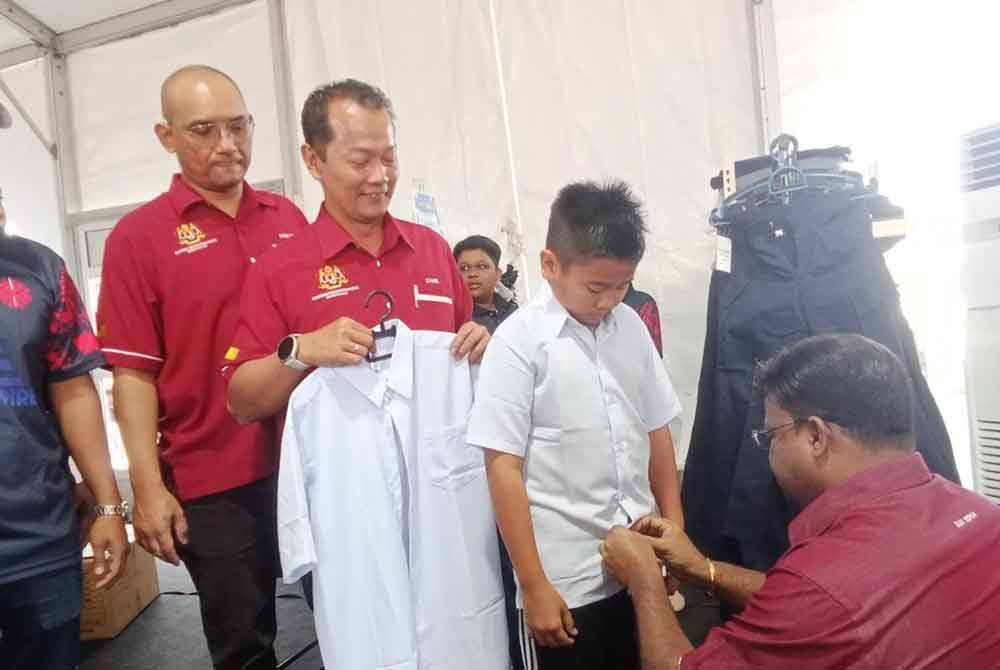 Veerapan (kanan) membantu seorang kanak-kanak mencuba pakaian sekolah pada karnival mini berkenaan pada Ahad.