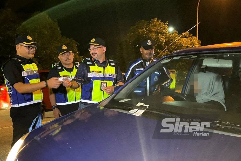 Mohd Misuari (kiri) memeriksa lesen memandu pengguna jalan raya semasa Penutup Operasi Khas Tahun Baharu Cina yang diadakan di JPJ Bukit Jawa, Pasir Puteh pada Ahad malam.