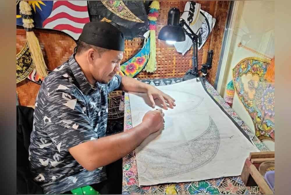 Megat Mayusif melakukan proses melakar corak wau di kertas putih.