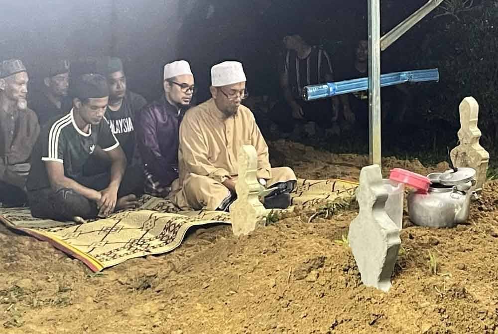Mohd (kanan) membaca talkin ketika pengebumian ahli keluarganya di Tanah Perkuburan Islam Kampung Tengkawang, Hulu Terengganu.