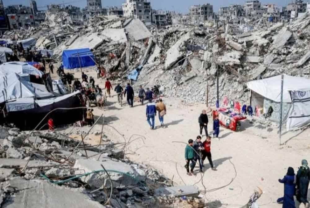 Penduduk Palestin berjalan di antara runtuhan bangunan yang musnah semasa serangan Israel.