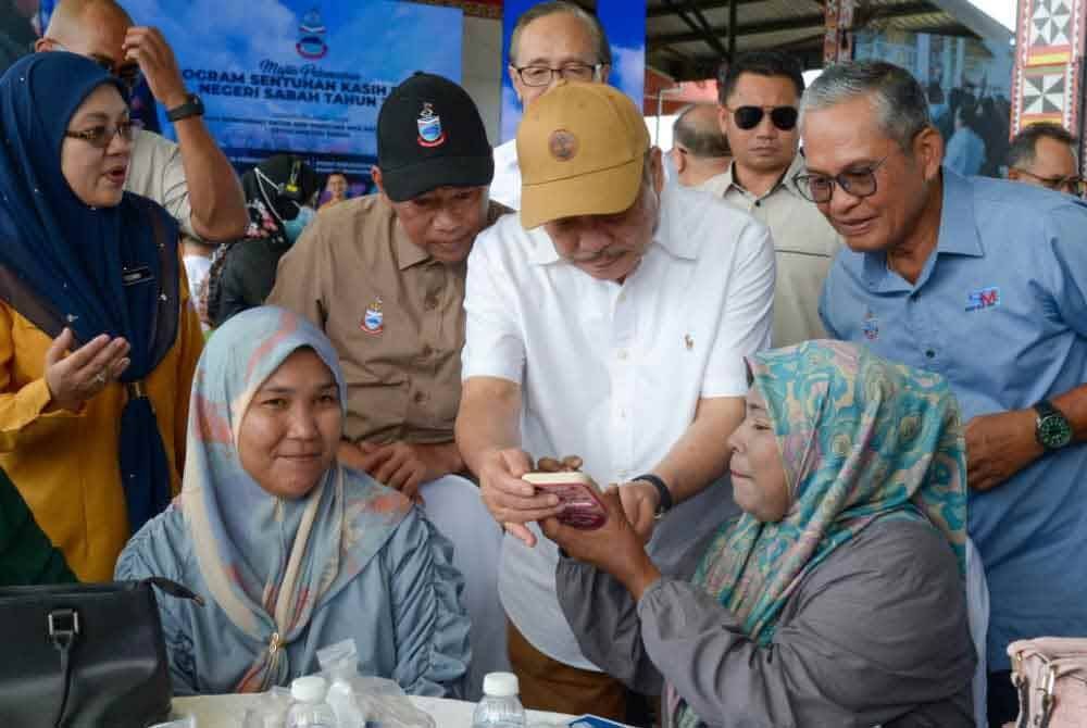 Seorang penerima menunjukkan telefon bimbitnya kepada Hajiji bahawa wang bantuan Syukur sudah dimasukkan ke dalam akaunnya.