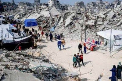 Penduduk Palestin berjalan di antara runtuhan bangunan yang musnah semasa serangan Israel.