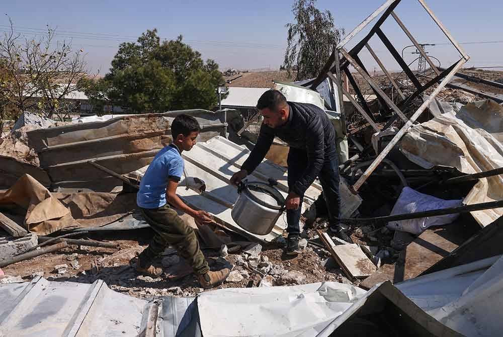 Seorang pemuda Palestin bersama anaknya mengumpulkan barangan yang masih boleh digunakan selepas rumah mereka dirobohkan.