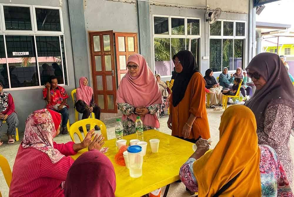 Salamiah (berdiri kiri) menyantuni mangsa banjir di Dewan Seri Gading.