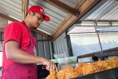 Alang sedang mengoreng ayam yang sudah diadun dengan tepung aduan di gerainya di Tanjung Lumpur. Foto Sinar Harian.