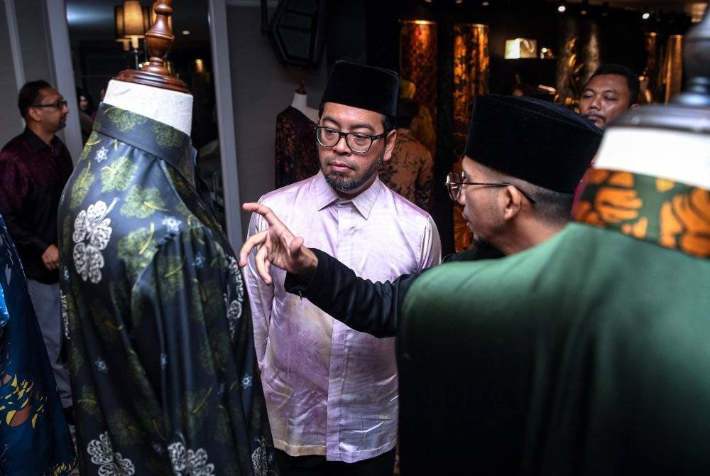 Zulkifli (kiri) mendengar penerangan mengenai Batik Nusa Malaysia dan Malaysia Madani daripada Pemilik Seni Masyaq, Ahmad Abdul Hadi Shamsul (kanan) semasa pelancaran Koleksi Kaligrafi Batik Jawi oleh Indah Atelier hari ini. Foto Bernama