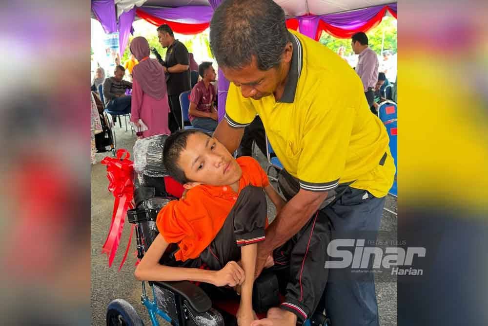 Mohd Nor Fezan (kanan) meletakkan Mohamad Hakimi (kiri) ke atas kerusi roda yang dimodifikasi. FOTO SINAR HARIAN-ADILA SHARINNI WAHID