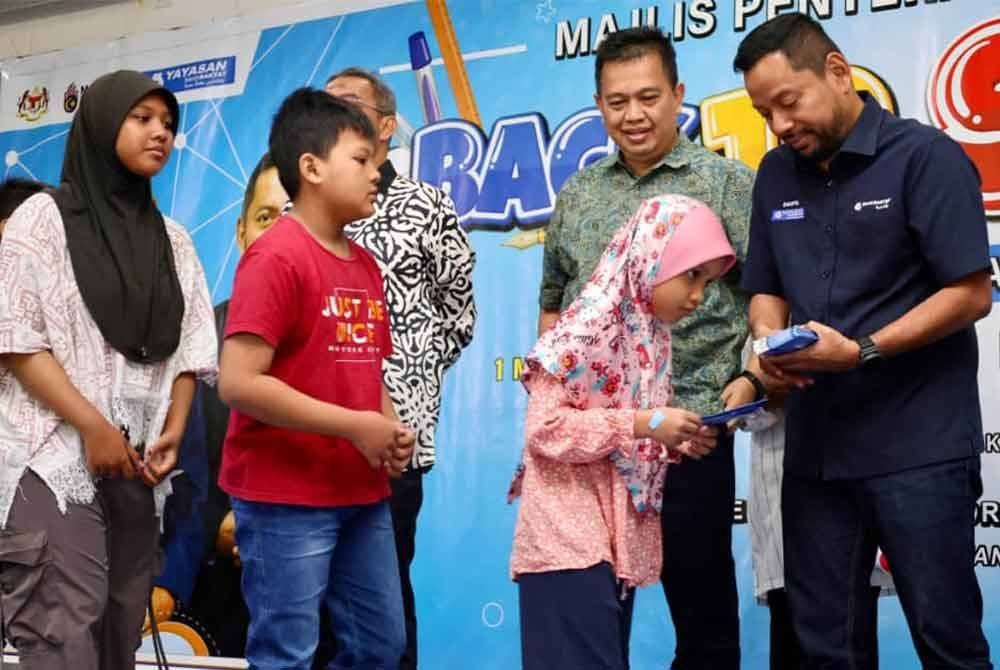 Syaiful Rizal (kanan) turut menyampaikan sumbangan kepada penerima sempena Majlis Perasmian Bantuan Persekolahan YBR di Dewan Inderawati di sini pada Sabtu.