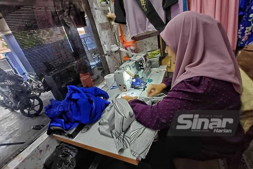Hasnuriza sedang menjahit baju yang ditempah pelanggan.
