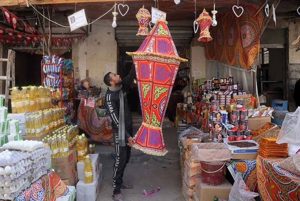 Seorang peniaga menggantung tanglung besar sempena menyambut bulan Ramadan di Khan Yunis, selatan Gaza. - AFP