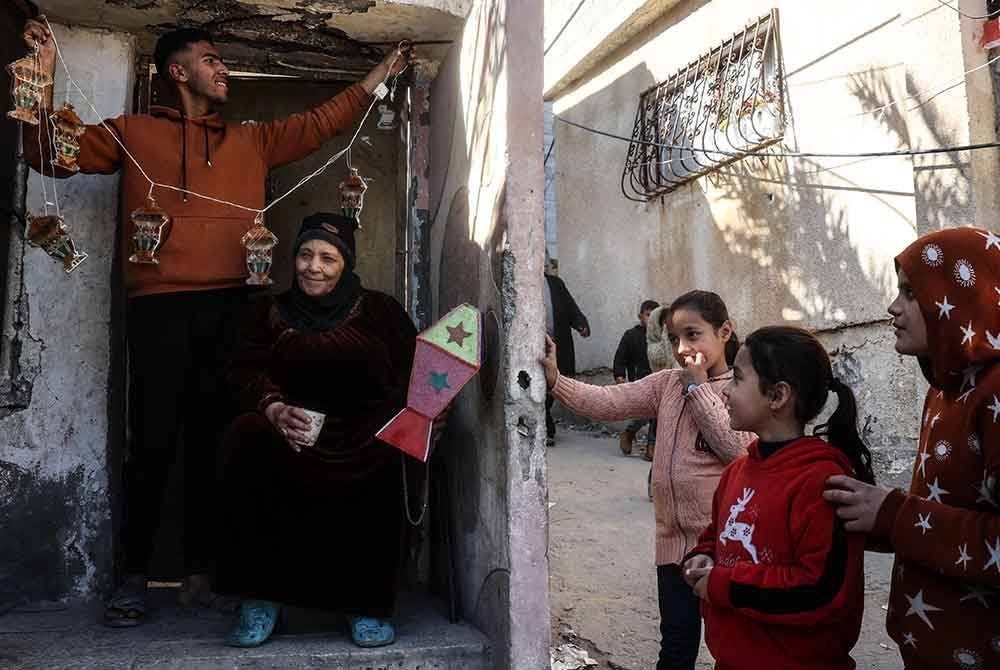 Kanak-kanak melihat seorang lelaki menggantung hiasan sempena menyambut bulan Ramadan di Khan Yunis, selatan Gaza. - AFP