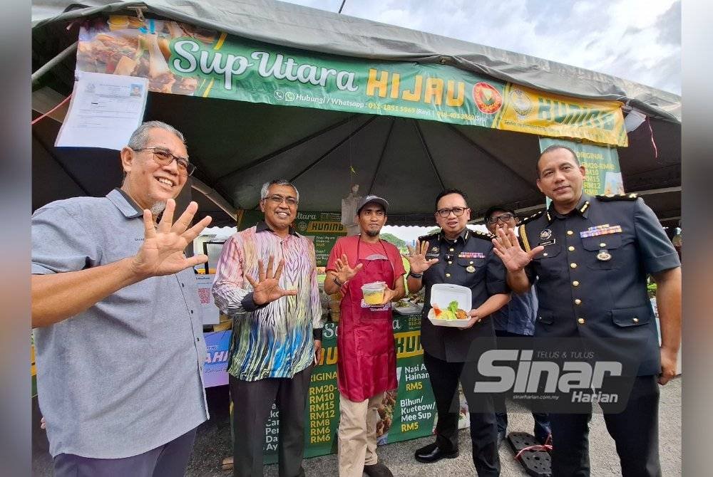 Kamalludin (dua dari kanan) menunjukkan tanda 5 simbolik menu rahmah yang dijual pada harga serendah RM5 di Bazar Ramadan Rahmah Taman Cempaka, Ipoh.