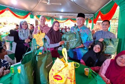 Syed Razlan (berdiri, dua dari kanan) menyampaikan sumbangan kepada komuniti Felda Gunung Besout 1 sempena majlis berbuka puasa pada Rabu.