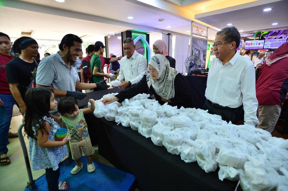 Dari kanan: Md Kamarzan, Sapna dan Suhaimi mengagihkan 500 bubur lambuk percuma kepada orang ramai di Kompleks PKNS Shah Alam pada Selasa.
