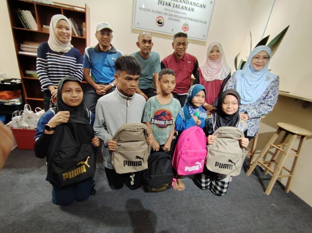 Anak-anak Rumah Ilmu, Chow Kit bergambar menunjukkan beg sekolah yang diterima bersama Suhaimi (belakang, tiga kanan), Ahli Pengurusan PKNS dan Pengurus Rumah Ilmu, Mohamad Azhan Mohamed Adnan
(belakang, tiga kiri).