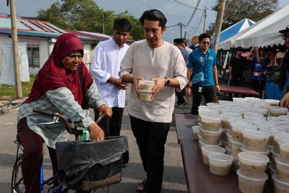 Adam Adli mengagihkan bubur lambuk kepada penduduk setempat sempena Majlis Peluncuran Santuni MADANI di Kampung Baru Penaga hari ini. Foto Bernama
