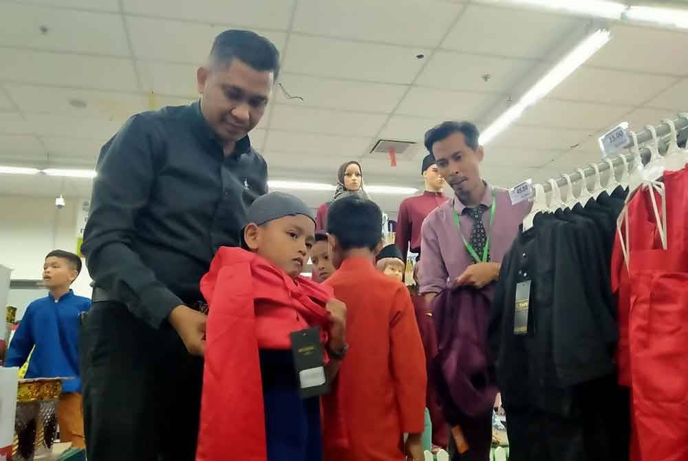 Mohd Syahrizal (kiri) membantu anak yatim memilih pakaian Hari Raya Aidilfitri sempena Program MBI Prihatin di Pasar raya Econsave Klebang di Ipoh baru-baru ini.