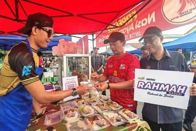 Muhammad Zahir (tengah) menyerahkan kad khas diskaun Rahmah kepada peniaga bazar Ramadan yang menawarkan menu Rahmah.