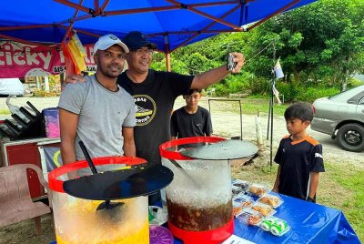Bekas pemain bola sepak kebangsaan, Mohammad Gopi Rizqi (kiri) kini bukan sahaja sibuk dengan jualan air balang di hadapan rumahnya di Kampung Api-Api di sini, tetapi turut sibuk melayan peminatnya yang hadir bukan sahaja membeli air tetapi berswafoto bersamanya. Foto Bernama