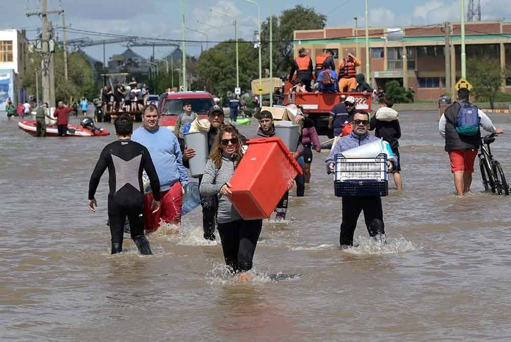 Orang ramai membawa barangan berjalan meredah air banjir sehari selepas ribut kuat melanda Bahia Blanca. Foto Agensi