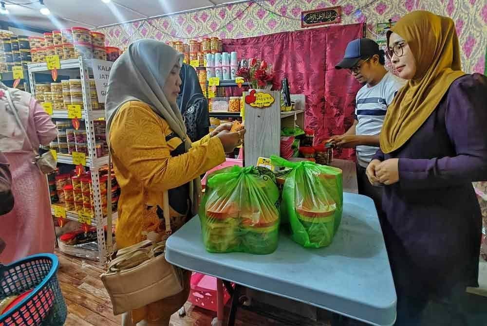 Azie (kanan) dibantu suaminya, Azley Alias, 42, mengushakan biskut raya rahmah di Kampung Gangsa di sini, pada Isnin.