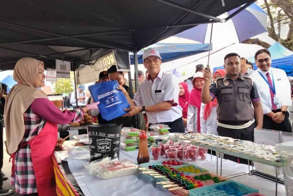 Dr Zaini (tengah) menyampaikan cenderamata kepada peniaga di bazar Ramadan di Dataran Kenanga